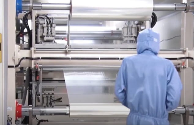 クリーンルームでフィルム製造機を監視する作業員