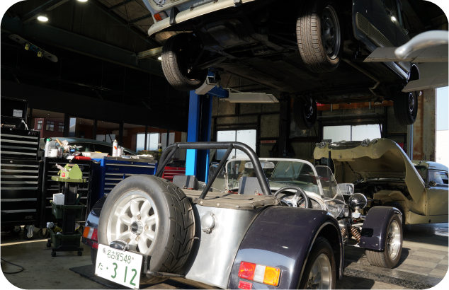 リフトに上げられたクラシックカーと、手前に停められたオープンカー